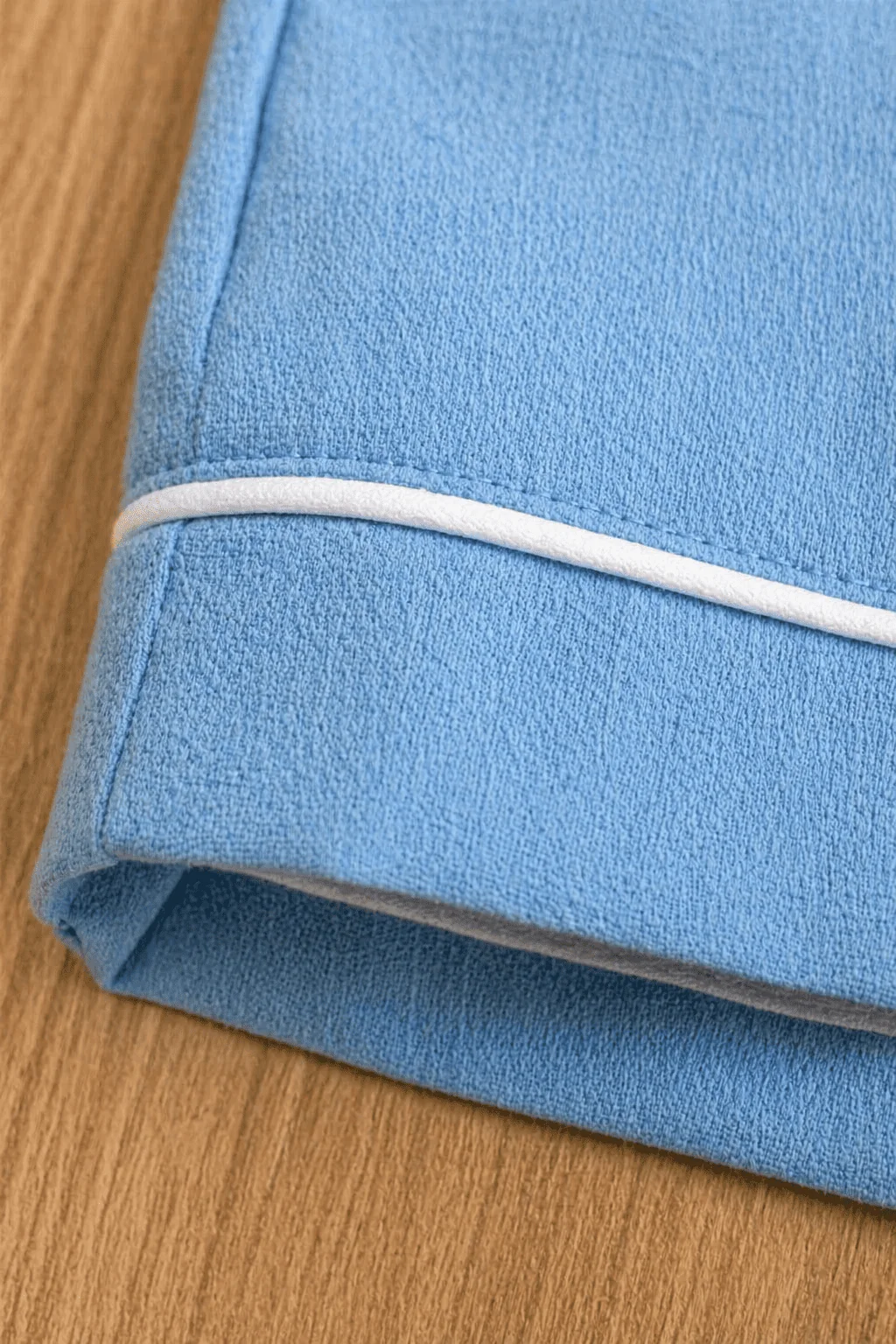 Detalhe macro do avesso da Jardineira Versátil em linho cru mostrando acabamento impecável — pesponto duplo, barra dobrada e overlock escondido